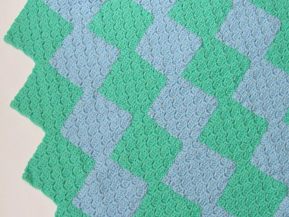 A partial section of a green and blue striped C2C crochet blanket, where the stripes are panels that look like connected diamonds