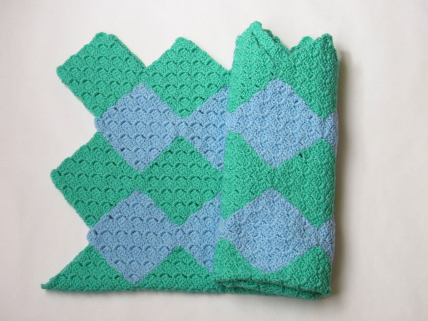 a partially folded up green and blue striped C2C crochet blanket, where the stripes are panels shaped like connected diamonds 