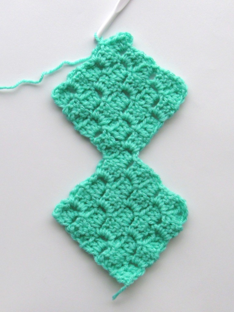 An image of two connected C2C crochet squares, that look like two connected diamond shapes, made from green yarn
