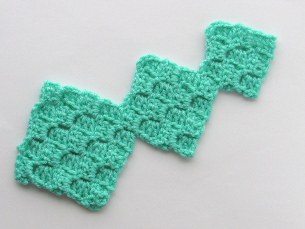 a panel of three connected C2C crochet squares, made of green yarn, where, starting from the left, each one is smaller than the other.