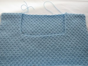 The incomplete neckline section of a blue C2C spider stitch sweater
