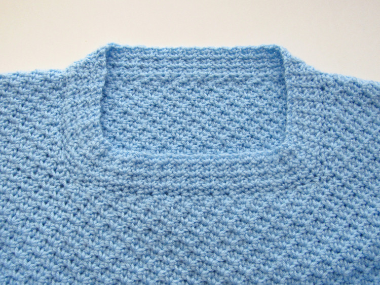 The completed neckline of a blue C2C spider stitch sweater, with straight rows of spider stitch edging