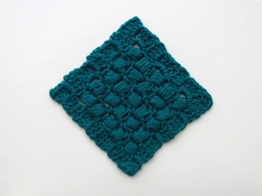 a green crochet c2c square, made of puff stitches in the middle and a border made of sets of 3 dc, oriented in a diamond shape