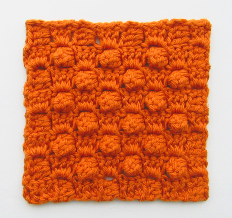a photo of an orange c2c crochet square that is made up of alternating rows of popcorn stitches and sets of 3 dc stitches, with a border made up of sets of 3 dc stitches