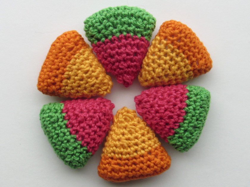 a closeup photo of crochet watermelon and lemon slices arranged in a cirlce. Each triangular in shape, with the watermelons having green and pink colors and the oranges having two shades of orange.