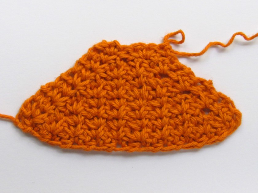 An orange spider crochet piece where the sides get narrower with each row.