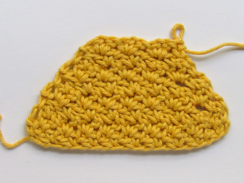 A yellow wattle stitch crochet piece where the sides get narrower with each row.