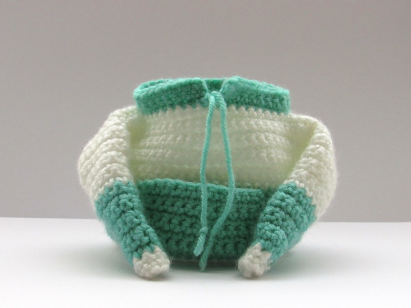 A photo of a small, crochet drawstring bag that looks like a sweater with a large front pocket. It is white with green stripes.