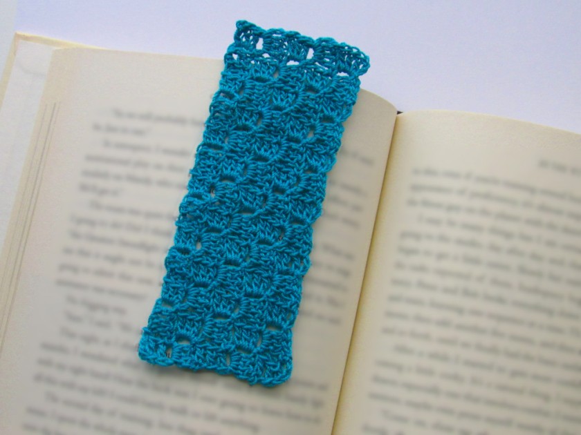 A photo of an open book with its text blurred with a green corner to corner/c2c crochet rectangular bookmark placed on the left side toward the middle of the book.