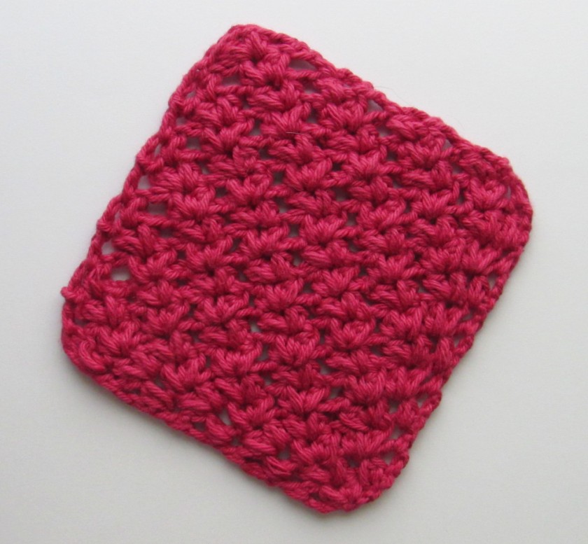 a photo of a bright red, crochet c2c V-puff stitch square oriented in a diamond position. The V-puff stitch is a reversible crochet stitch made up of two puff stitches separated by a ch-1 space.