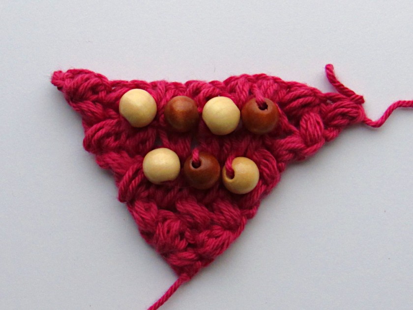 an image of a red c2c crochet bean stitch piece with several brown beads in it