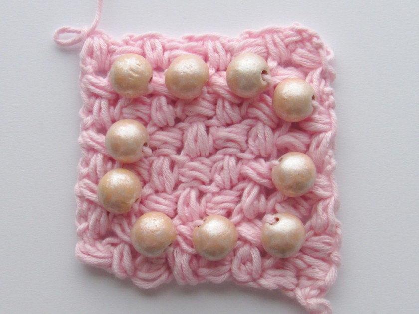an image showing a pink c2c crochet bean stitch square with pink beads in it that form a border around the piece